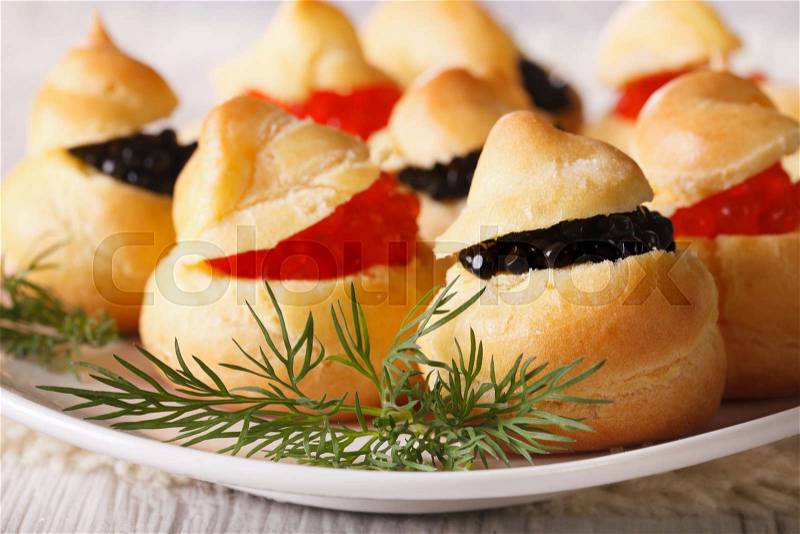Finger food: profiteroles stuffed with red and black caviar on a plate close-up. horizontal , stock photo