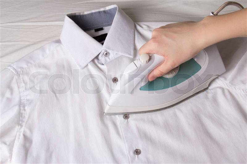 Iron in female hand ironing white cotton shirt, stock photo
