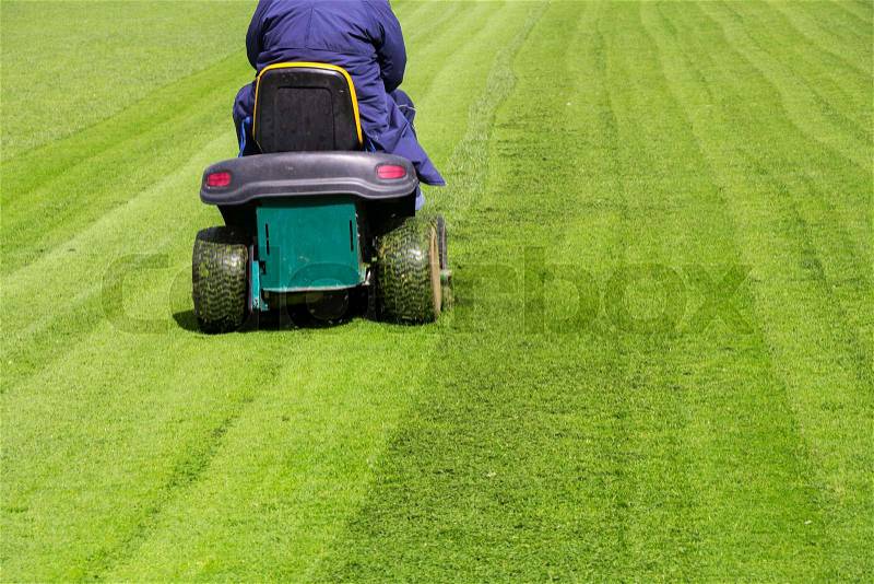Mowing the grass motor lawn mower on a football field, stock photo