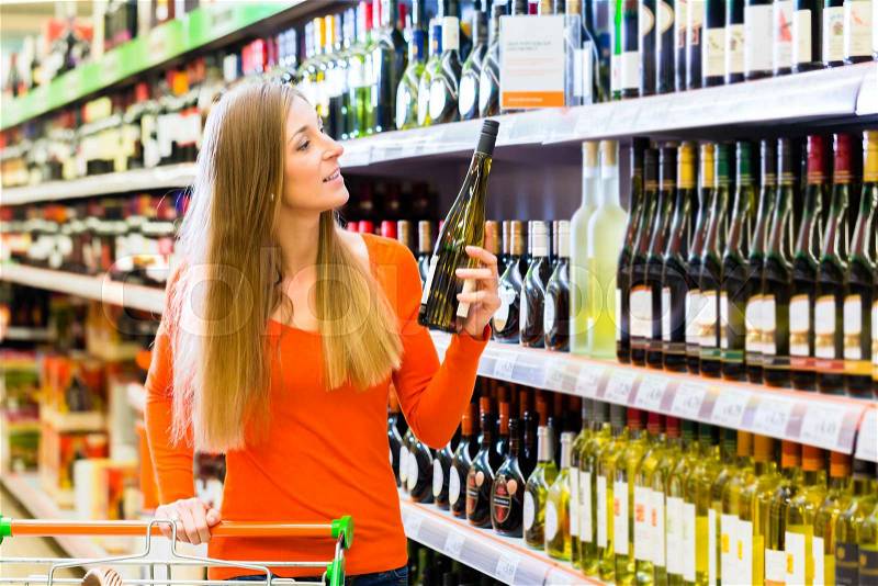 Woman buying wine in supermarket store, stock photo