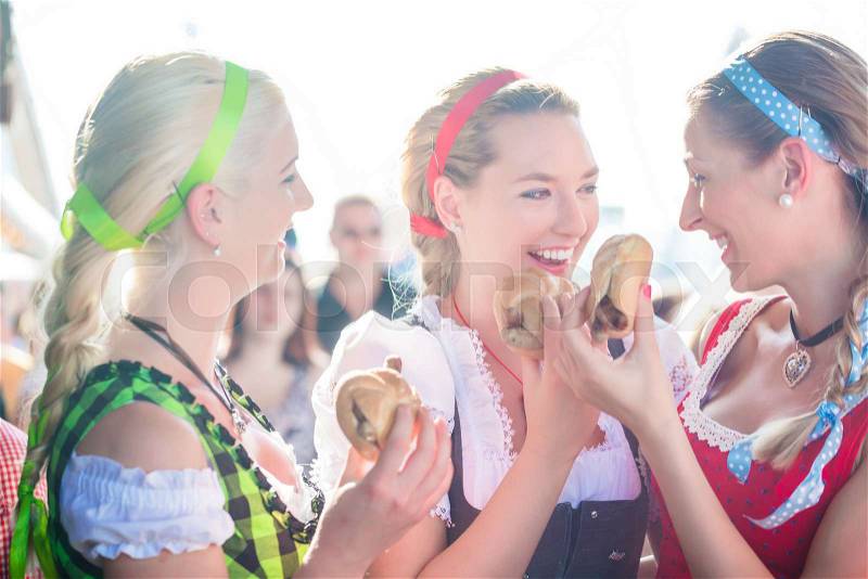 Friends visiting together Bavarian fair in national costume eating grilles sausage in bread roll, stock photo