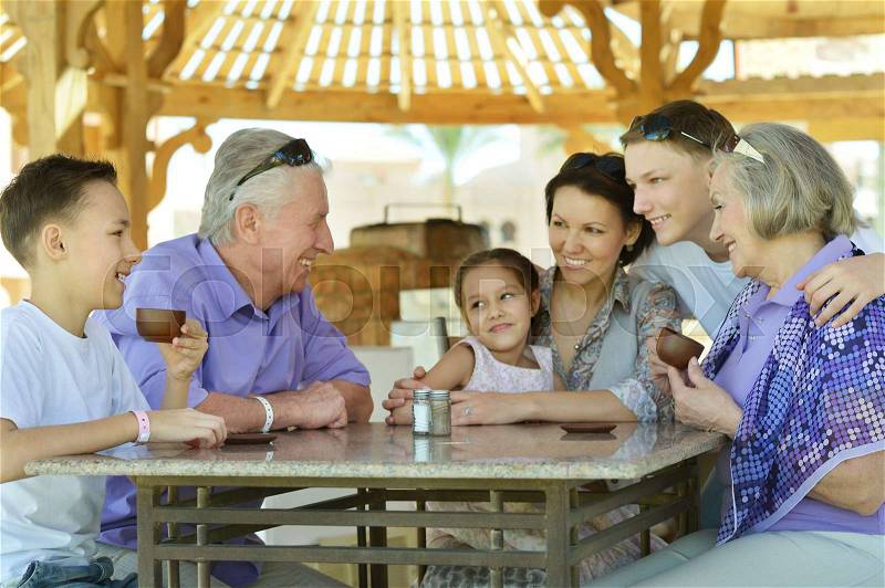Happy family drinking tea at table outdoors in summer time, stock photo
