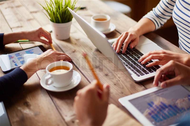 People using different devices at one table, stock photo