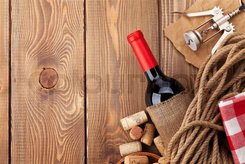 Red wine bottle, corks and corkscrew over wooden table background. Top view with copy space, stock photo