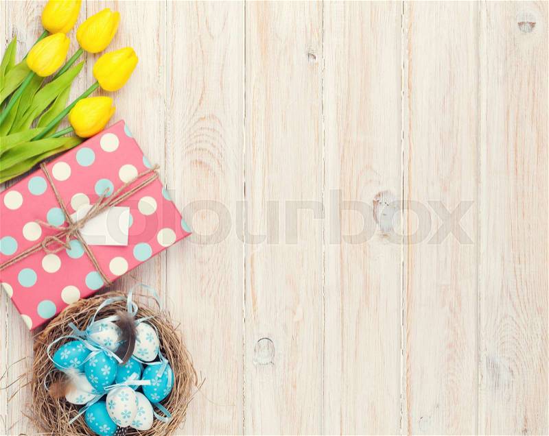 Easter background with blue and white eggs in nest, yellow tulips and gift box. Top view with copy space. Vintage toned, stock photo