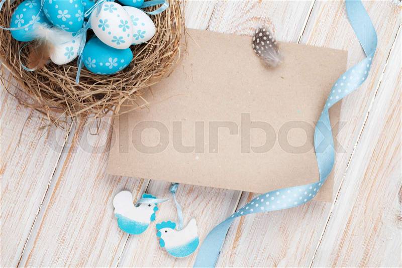 Easter greeting card with blue and white eggs in nest and decor. Top view with copy space, stock photo