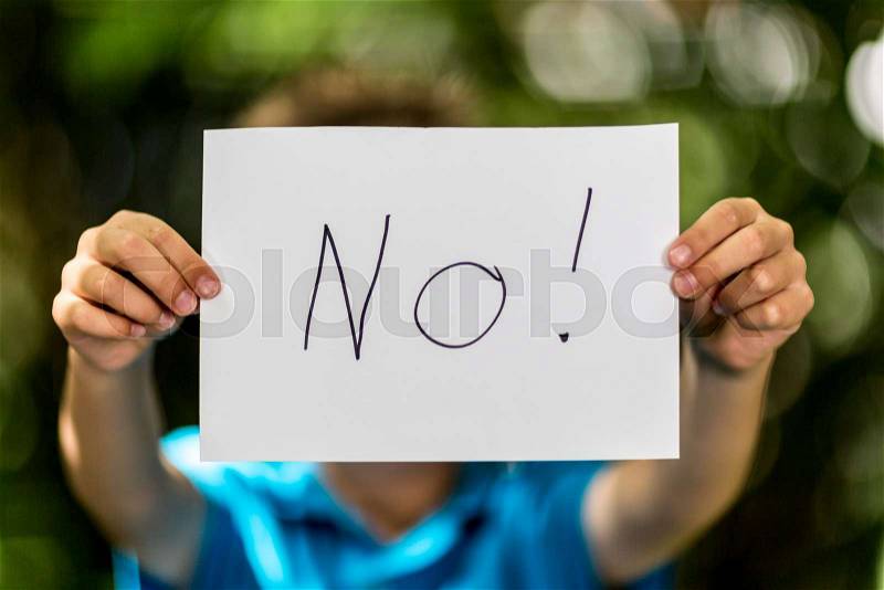 Blurred boy holding a piece of paper with the word No in front of her, stock photo
