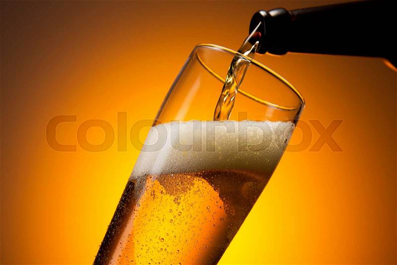 A bottle of beer pouring out in to a glass with dew drops on orange sumer background. Taken in Studio with a 5D mark III, stock photo