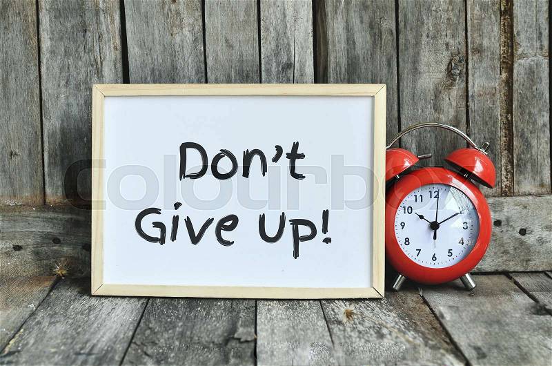 Don\'t give up message note on white board with red retro clock on wooden background, stock photo