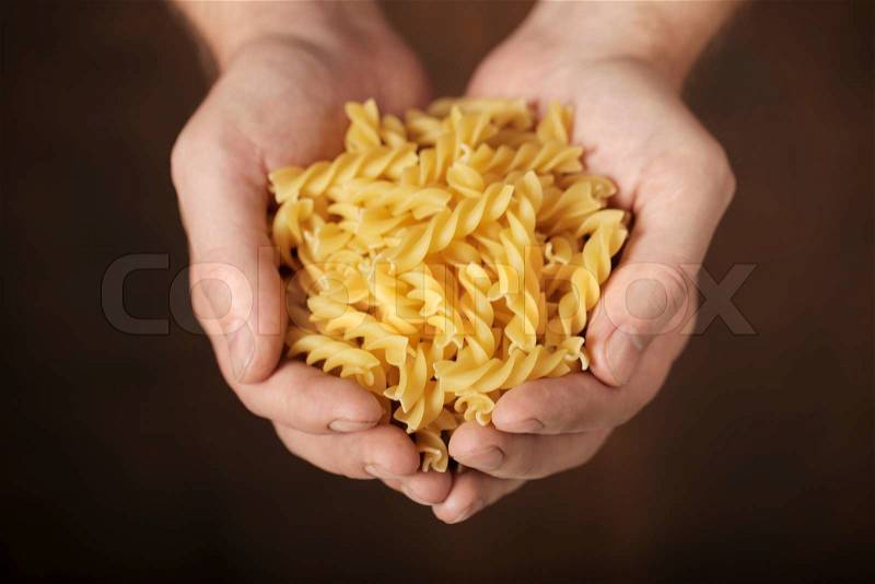 Man holding uncooked fusilli pasta in his hands. Very short depth-of-field, stock photo