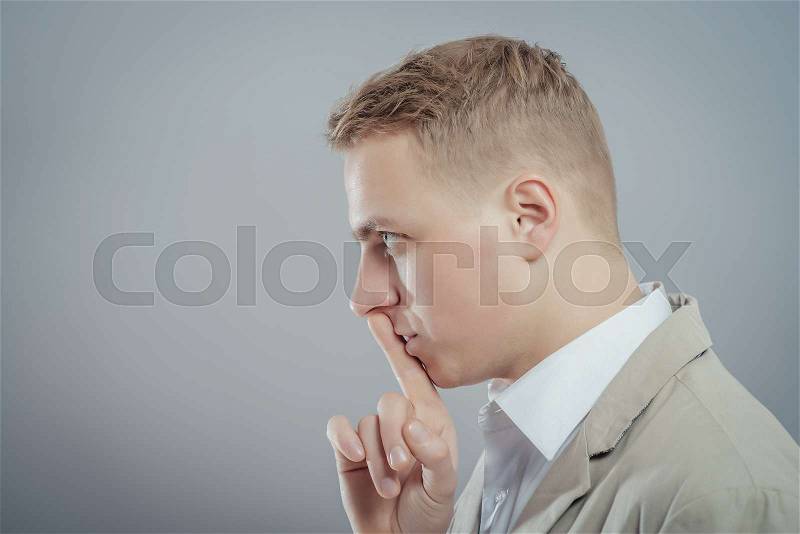 Closeup portrait young serious businessman placing finger on lips saying, shhh, be quiet, silence, isolated grey background. Facial expression, human emotions, sign, symbol, body language, perception, stock photo