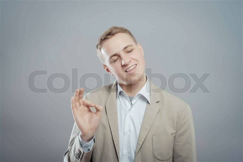 Gesturing OK sign. Cheerful young man in shirt gesturing OK sign while standing against grey background, stock photo