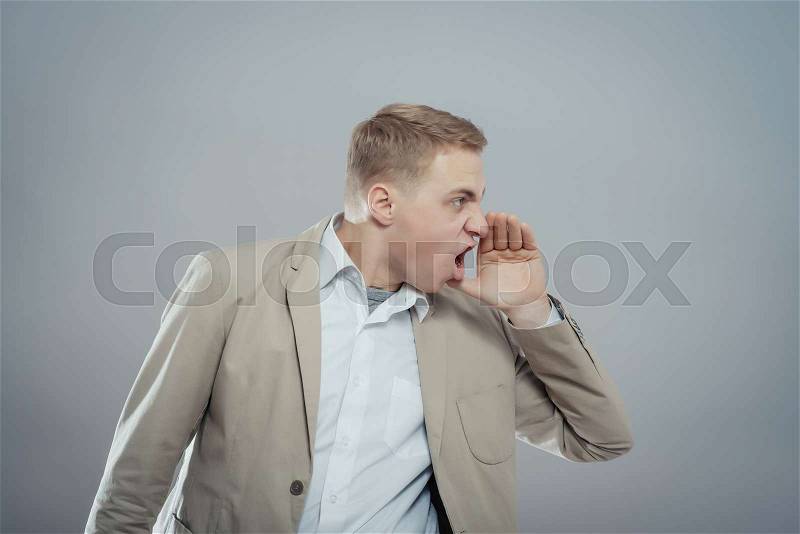 Portrait of a young man shouting loud with hands on the mouth, stock photo