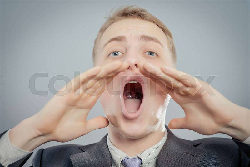 Portrait of a young man shouting loud with hands on the mouth, stock photo