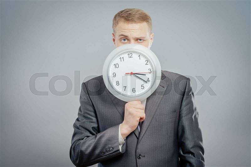 Portrait of standing businessman wearing suit and hiding his face behind clock, stock photo