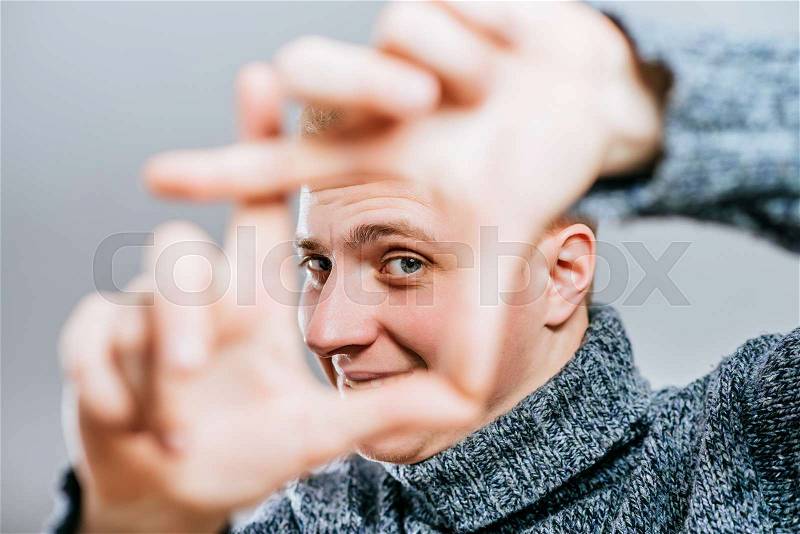 Handsome blond young man doing frame gesture with fingers, looking at camera through it, stock photo