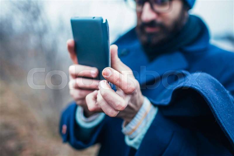 Adult man taking a picture with smart phone. Outdoor shot in nature, stock photo