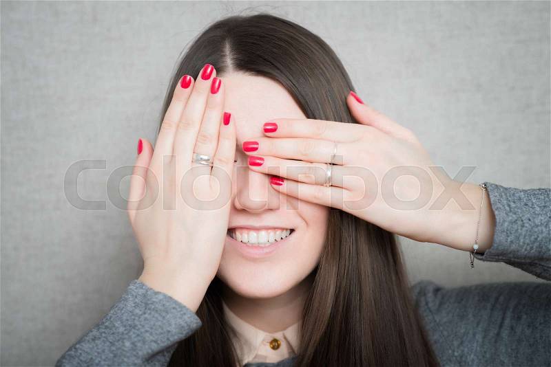 Smiley woman covering her eyes by hands over dark background, stock photo