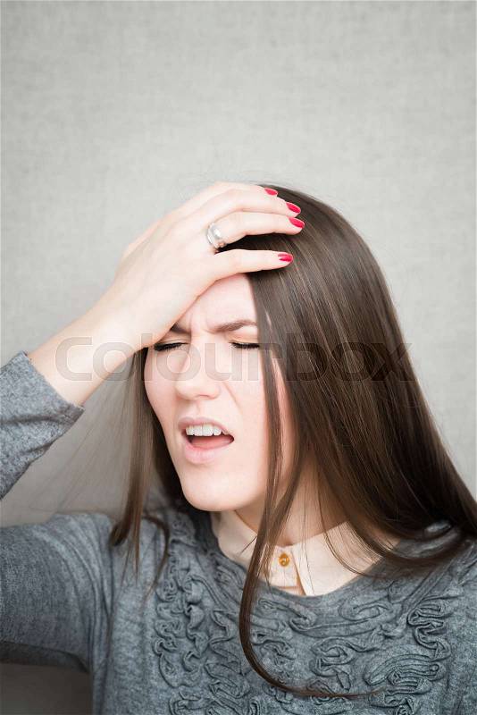 Closeup portrait headshot stressed sad young housewife, woman, employee having migraine, tension headache isolated on grey wall background. Human face expression emotion reaction, attitude, stock photo