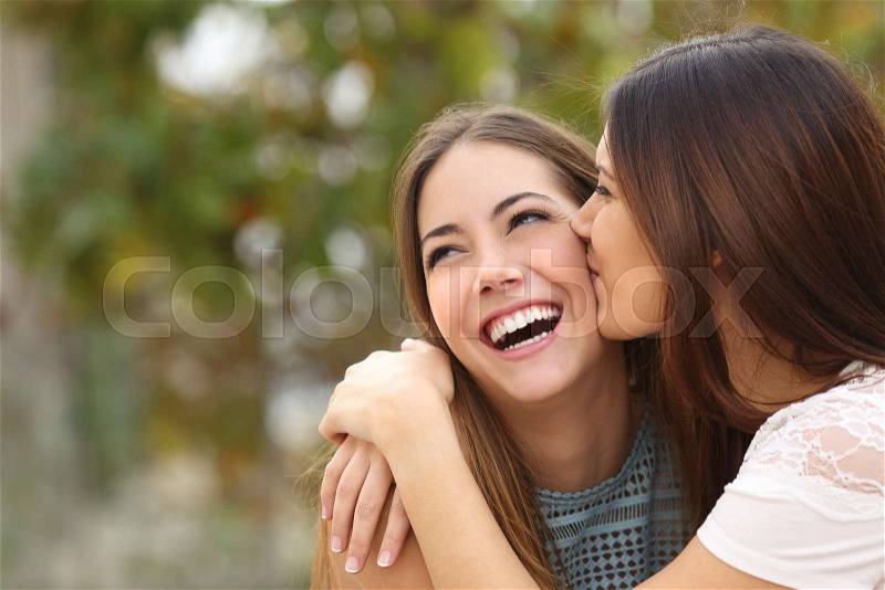Two funny affectionate women friends laughing and kissing outdoors, stock photo