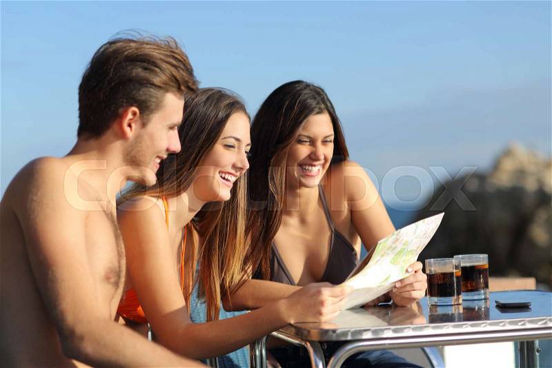 Friends on summer vacations consulting a guide in an hotel terrace on the beach, stock photo