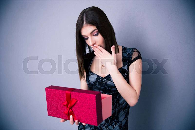 Amazed woman opening gift box over gray background. Wearing in dress. Looking on present, stock photo