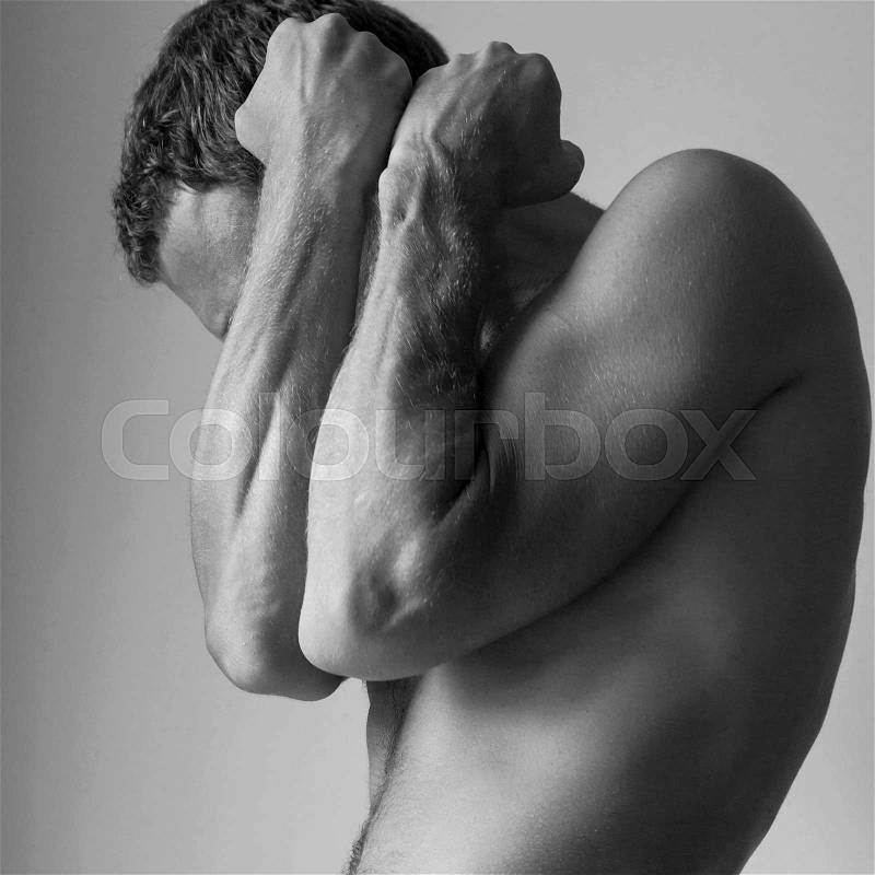Strong young Caucasian man hides behind his blocking hands, black and white studio photo, stock photo
