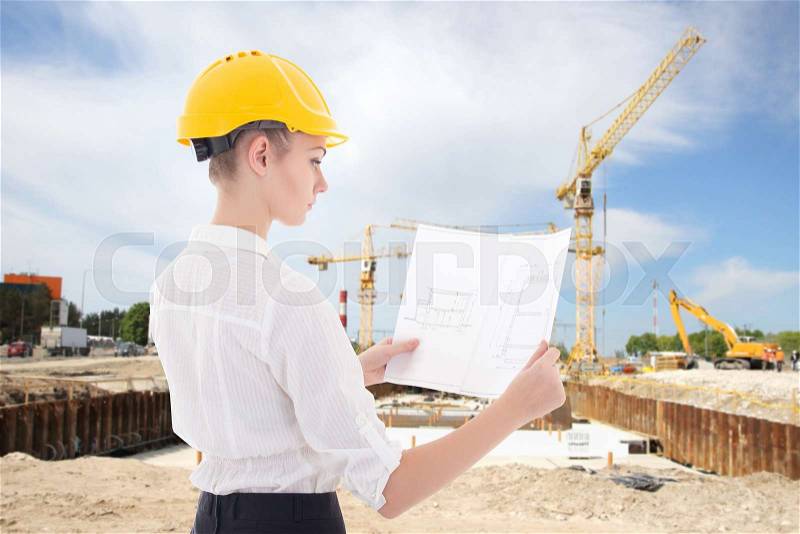 Young business woman architect in yellow builder helmet with building plan at construction site, stock photo