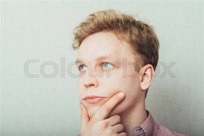 Portrait of the young thinking man looks up with hand near face, stock photo