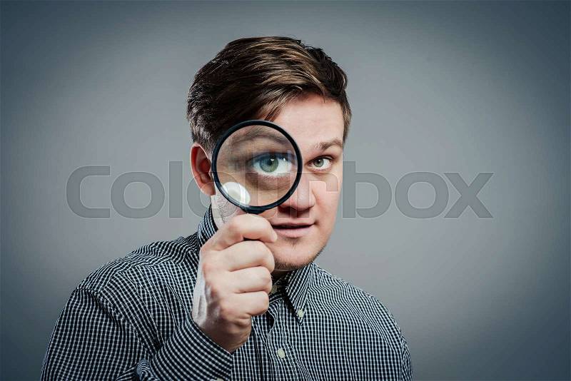 Funny image of a adultman with a magnifying glass, one eye is enlarged, stock photo