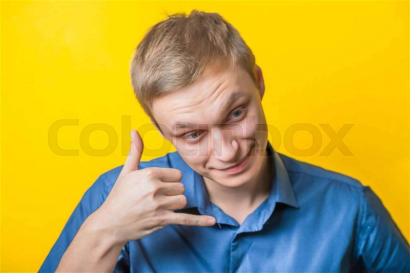 Young man in a blue shirt on a yellow background. Laughing shows call me. gesture. photo shoot, stock photo