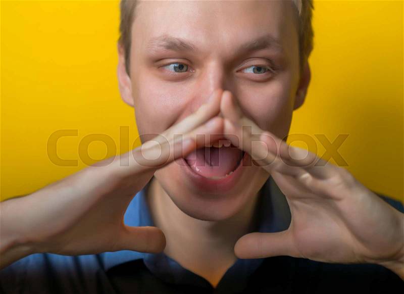 Two hands covering her mouth on the sides show a loud cry. young guy on a yellow background. Photo. Men loudly calling someone, stock photo
