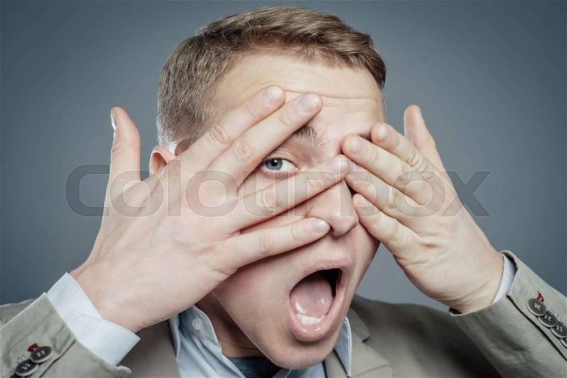 Expressions. Handsome young man in suit feeling fear with open mouth and closing eyes with hands, stock photo