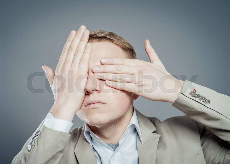 Portrait of a young man covering his eyes with hands, stock photo