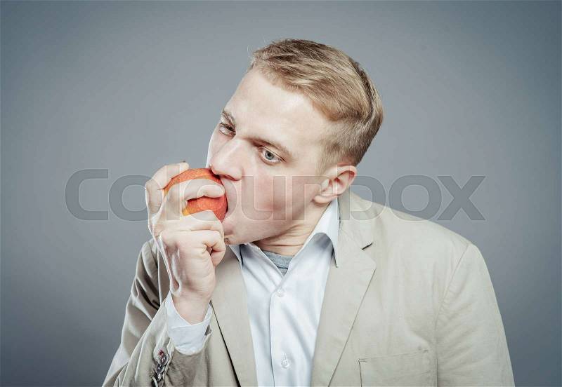 Cheerful beautiful man eating apple, isolated over gray background, stock photo