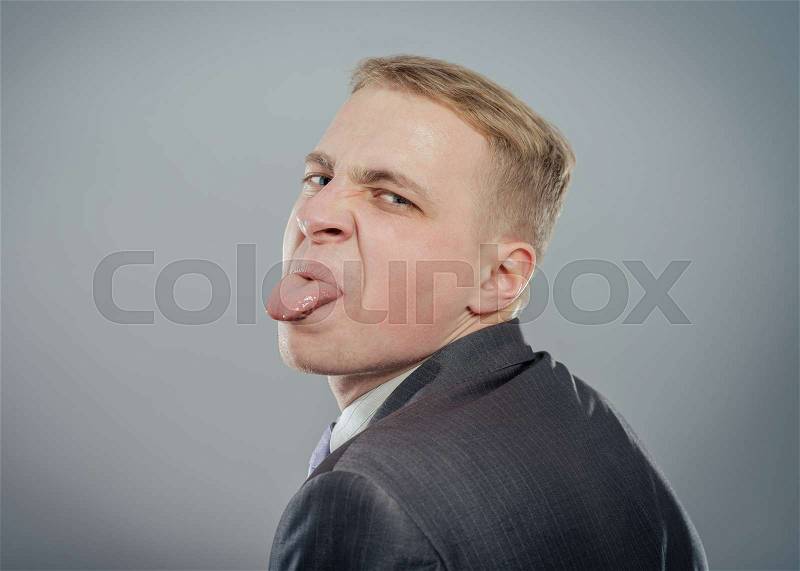 Closeup portrait funny annoyed young childish rude bully man sticking his tongue out at you camera gesture, isolated gray background. Negative emotion facial expression feelings, signs, symbols, stock photo