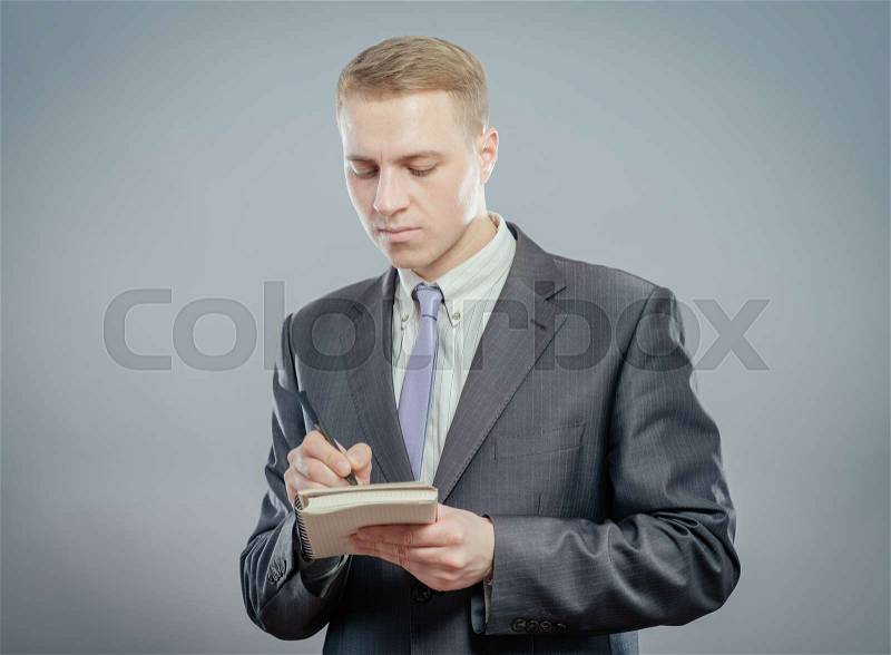 Businessman in suit writing on empty notepad (notebook), stock photo