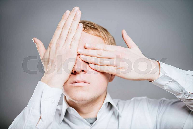 Closeup portrait of young guy, man, student, boy, worker, employee, closing eyes with hands, can\'t see, hiding, isolated background. See no evil concept. Human emotions facial expressions, stock photo