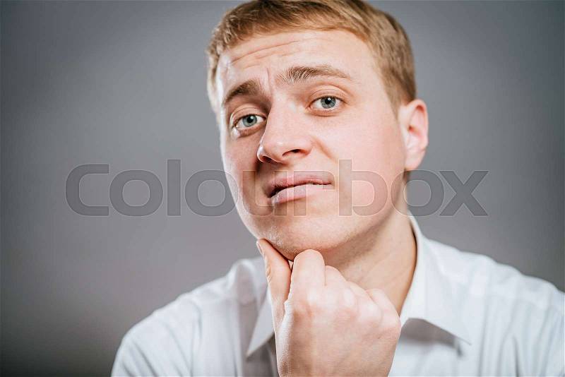 Young man thinks thinks. head resting on his hand, looking into the camera. Gesture, stock photo