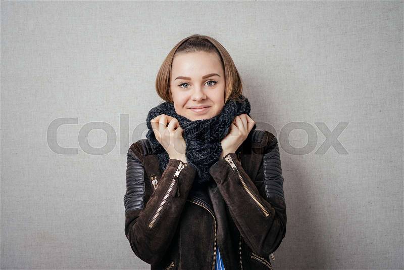 It is so cold. Frozen young women covering face with turtleneck while standing against grey background, stock photo