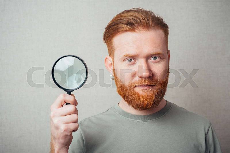 Young hipster red bearded man with magnifying glass, stock photo