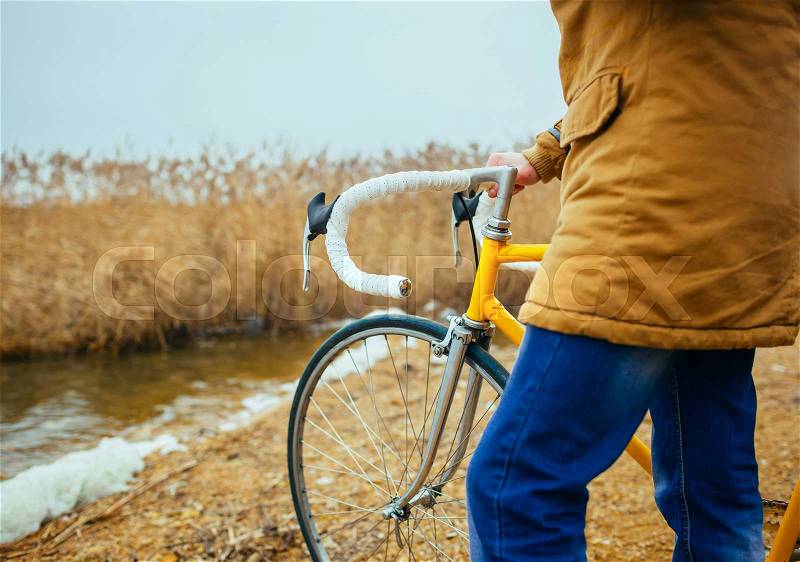 A young man with hands on the steering wheel of bicycle near the lake, stock photo