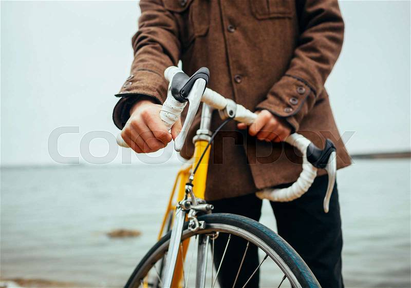 A young man with hands on the steering wheel of bicycle near the lake, stock photo
