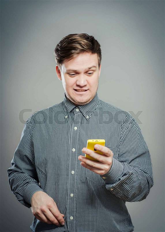A confused young man looking at mobile phone, stock photo