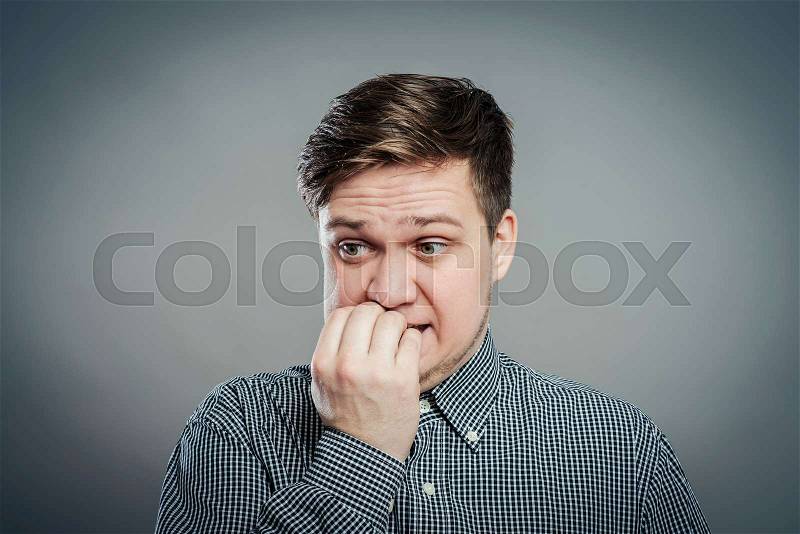 Portrait of thinking man with fingers in mouth, biting fingernail. Negative emotion, facial expression, stock photo