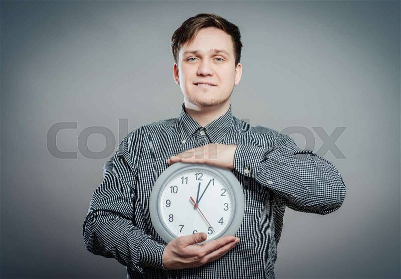 Young Man Holding A Clock On Gray Background, stock photo