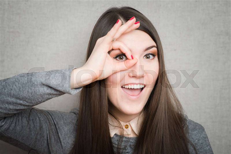 Young happy woman holding her hand over her eye as glasses and looking through fingers, stock photo