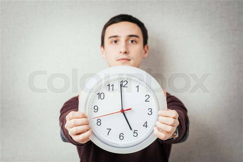 Portrait Of A Young Man Holding A Clock On Gray Background, stock photo
