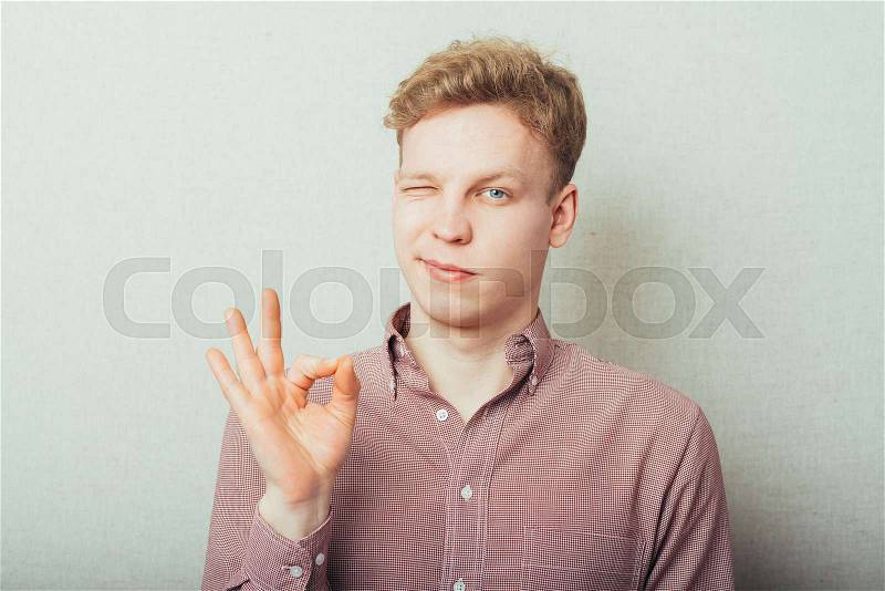 Gesturing OK sign. Cheerful young man in shirt and tie gesturing OK sign while standing against grey background, stock photo