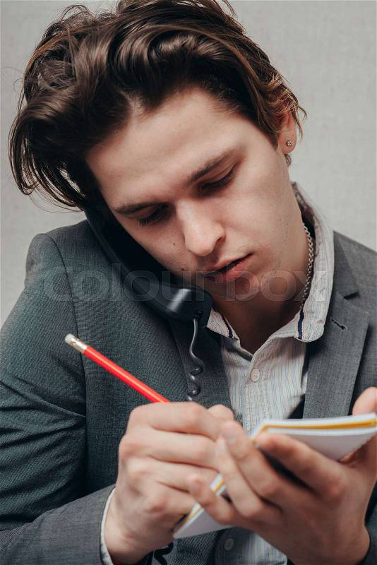 Concentrated on work. Confident young man talking on the landline telephone and writing something in note, stock photo